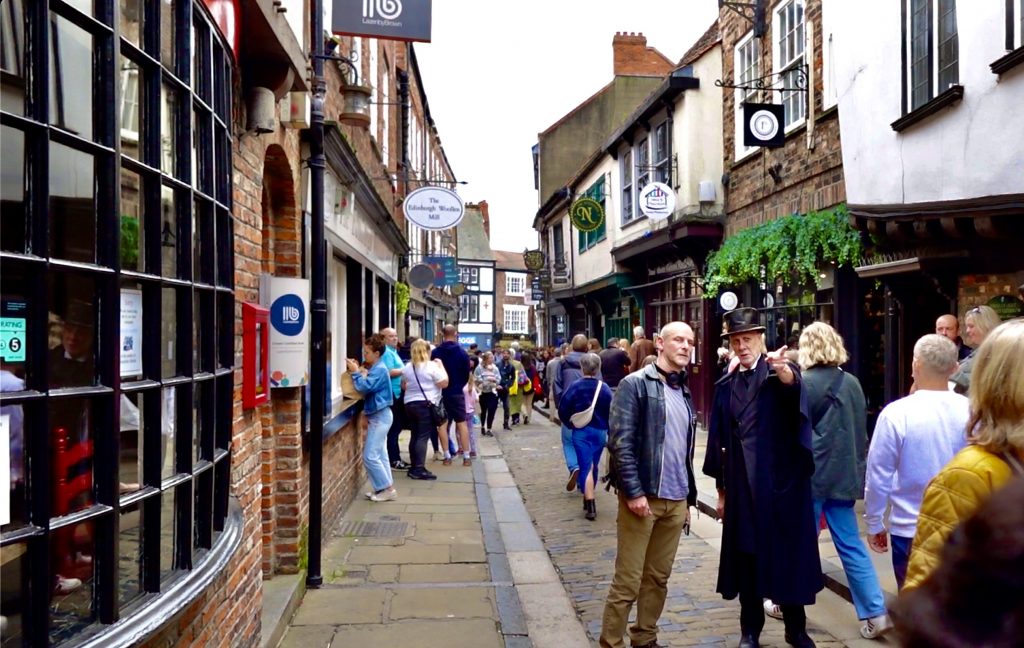 A crowded street with a man in a suit pointing and another man listening as the focus.
