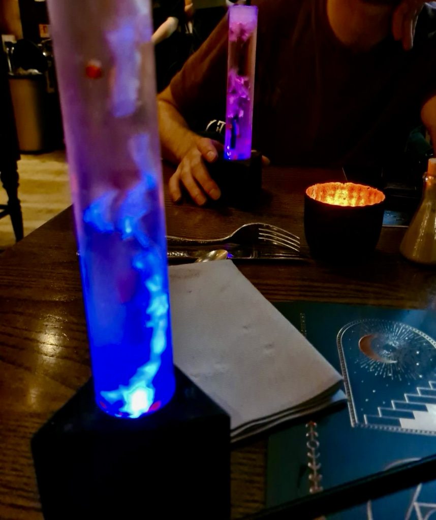 Two tall glasses containing a bubbly cocktail and lights.